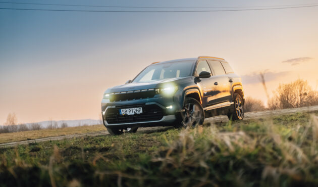 Ciemnoniebieski SUV Jeep Compass stojący na wiejskiej drodze o zachodzie słońca z włączonymi światłami przednimi.