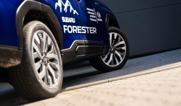 Boczny profil niebieskiego Subaru Forester pokazujący dwa koła z alufelgami oraz napis na drzwiach.
